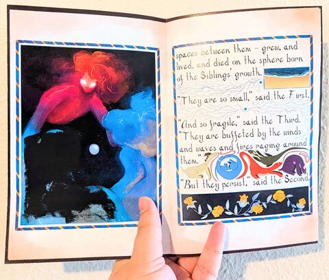 Photo of an open copy of the zine. The right page is text with marginalia on it and the left page is a full-page illustration with one of the figures blocked out with acrylic paint.