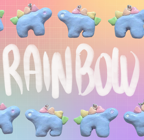 Alternating stegosaurus charms arranged in two rows along the top and bottom of the image. All of the charms are pastel blue with rainbow-colored back plates, but two have white eyes and the other two have pastel purple eyes. "Rainbow" is handwritten in white in the middle of the image between the two rows. The background is an unevenly faded white grid overlaying a pastel rainbow gradient.